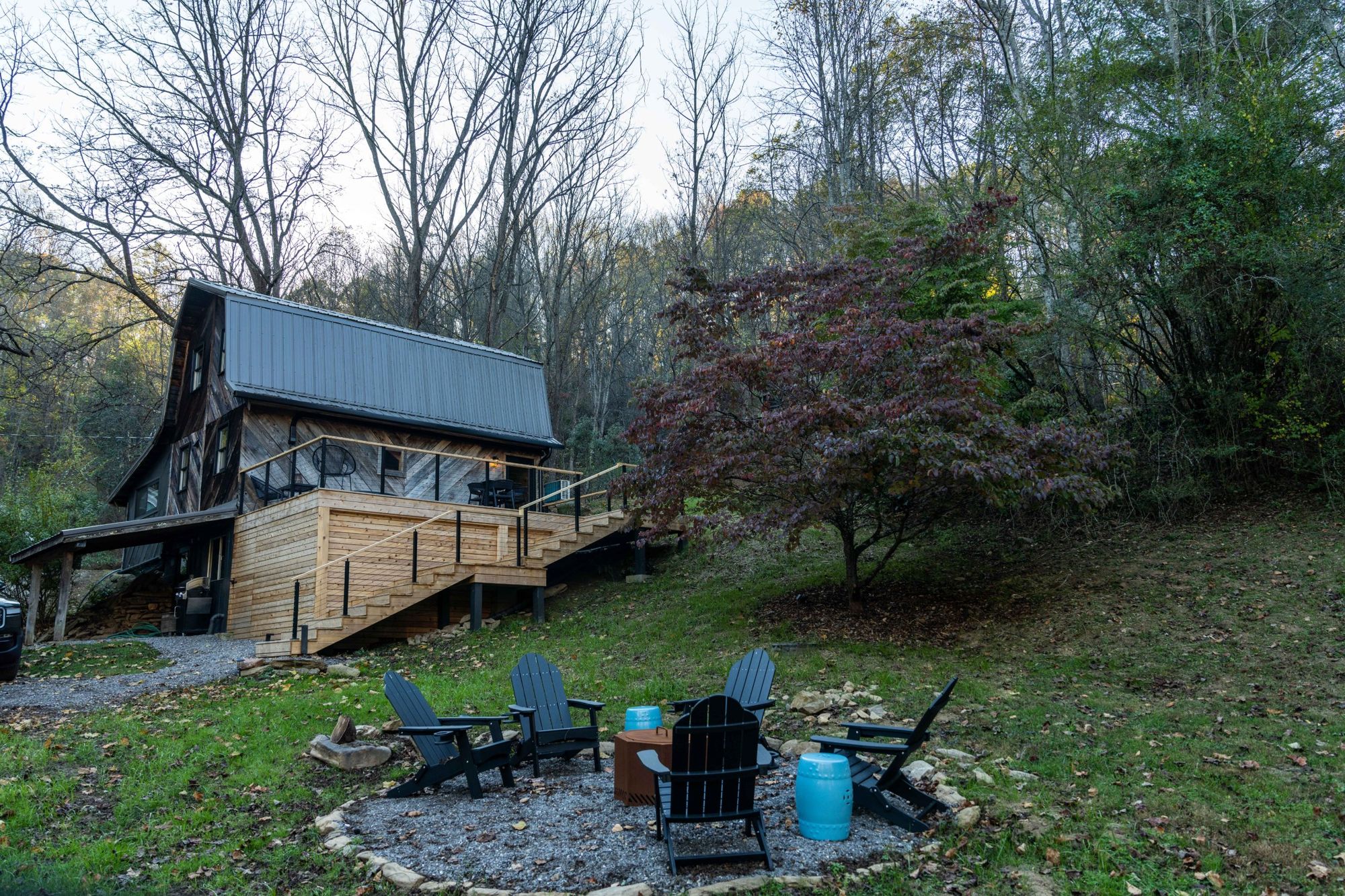Daisyfield Cabin on its wooded hillside, with the deck, stairs and fire pit below
