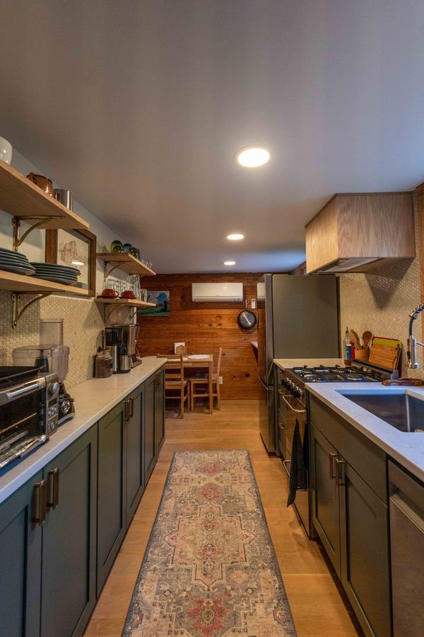 Galley kitchen with green cabinets, gas range and runner rug